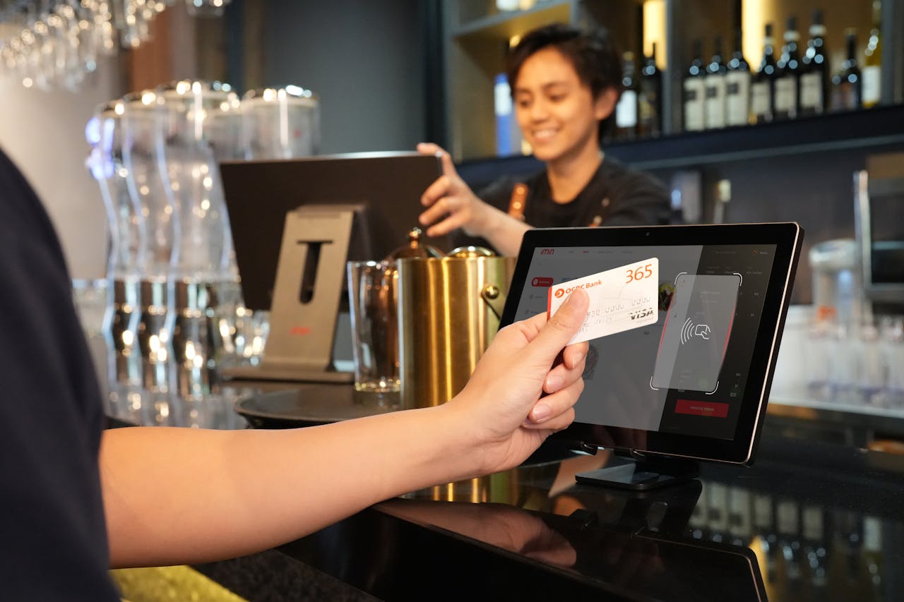 about-us Person using contactless credit card payment at a modern bar, assisted by a cashier.