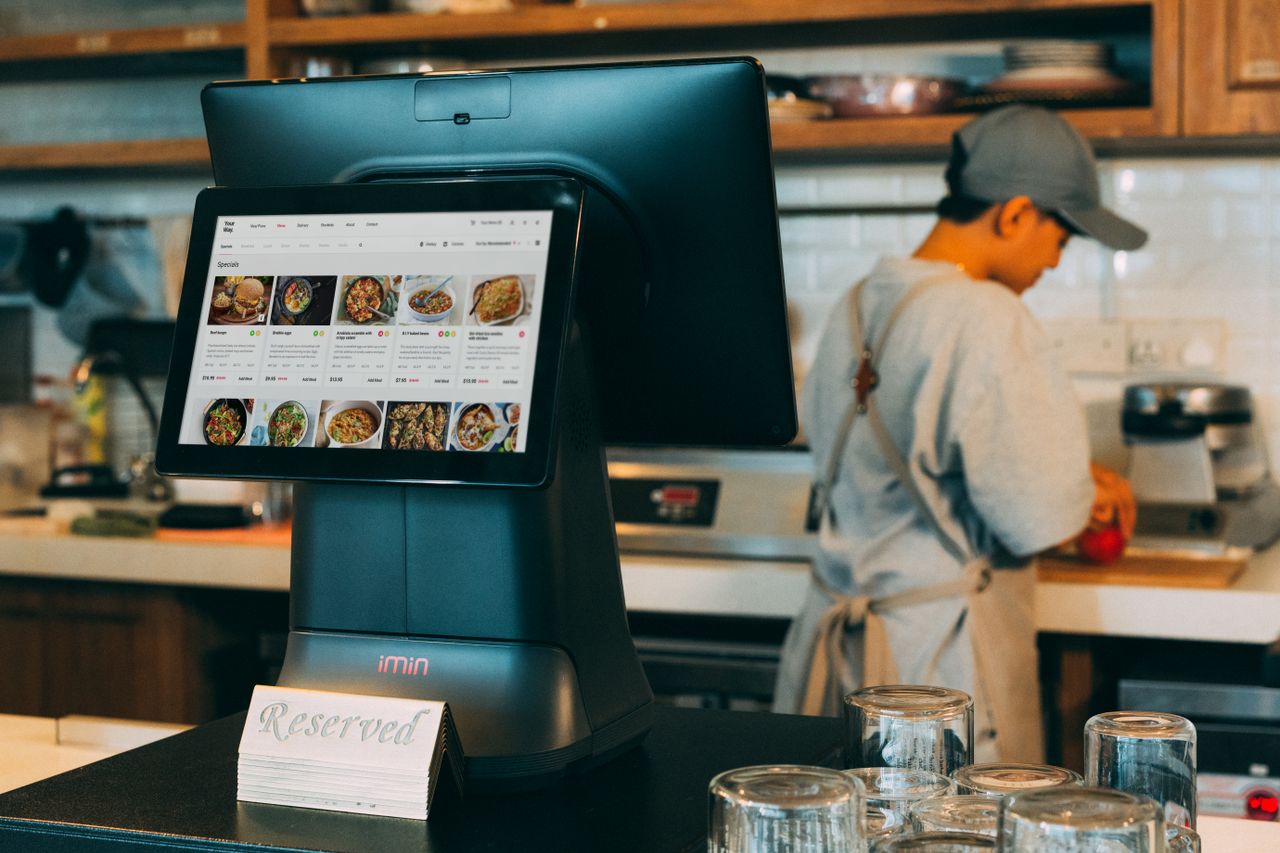 services-03 Digital ordering system in a restaurant kitchen with a touchscreen display and a chef at work.