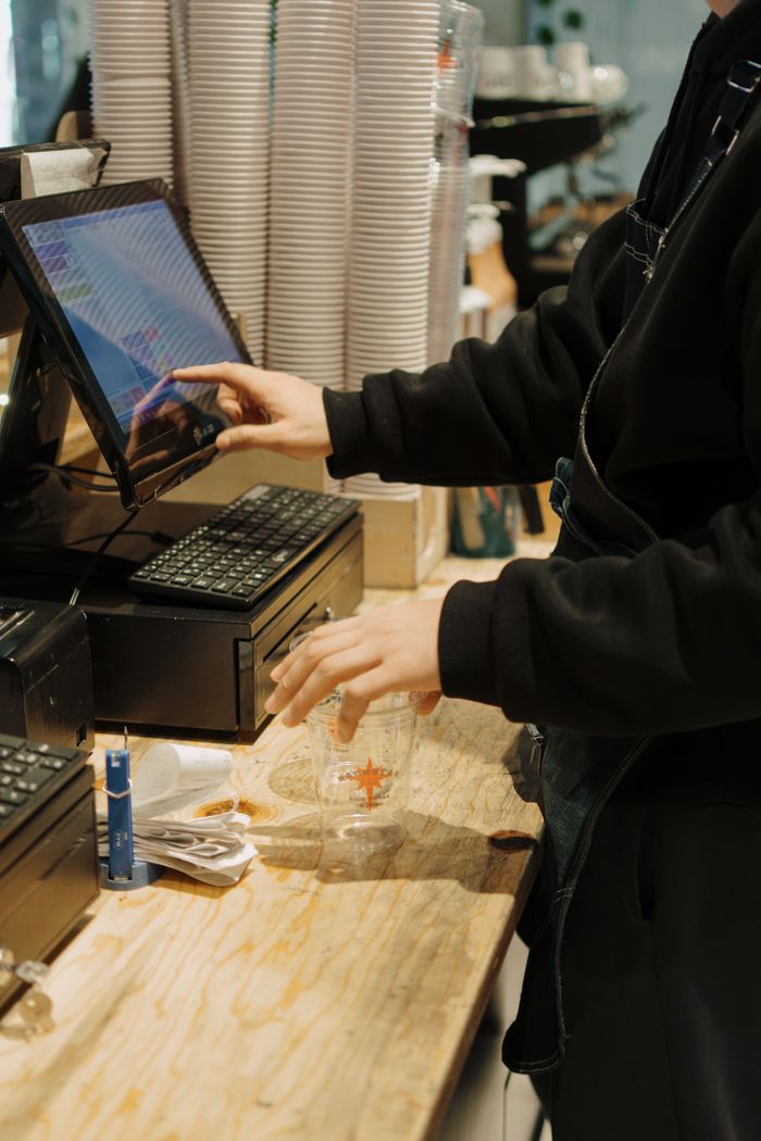 services-02 A barista operates a touchscreen register while preparing drink orders at a bustling coffee shop.