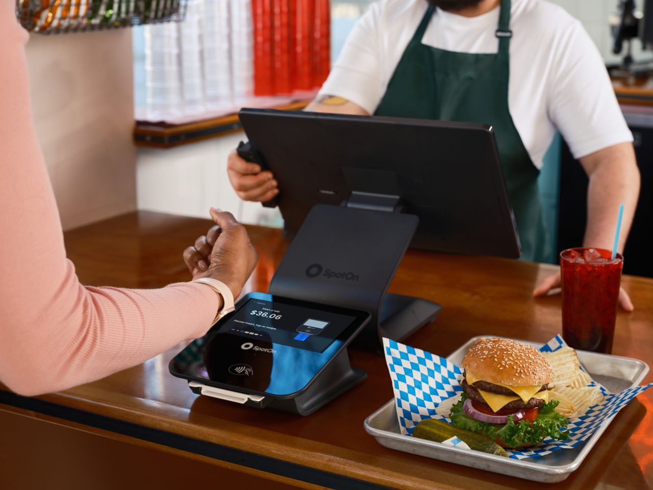 about-us-01 Customer using contactless payment at a restaurant counter with a burger and drink.